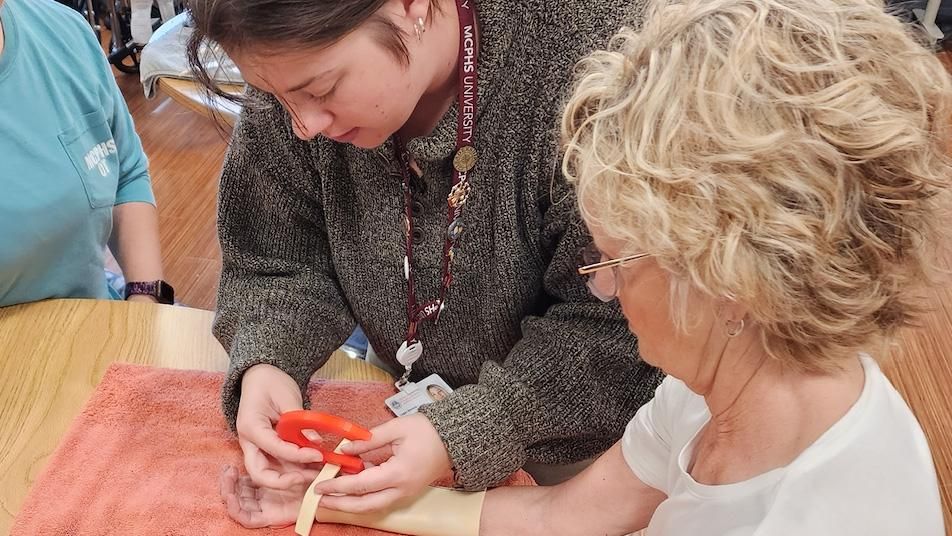 An OT student puts a 3D printed device on a woman's wrist.