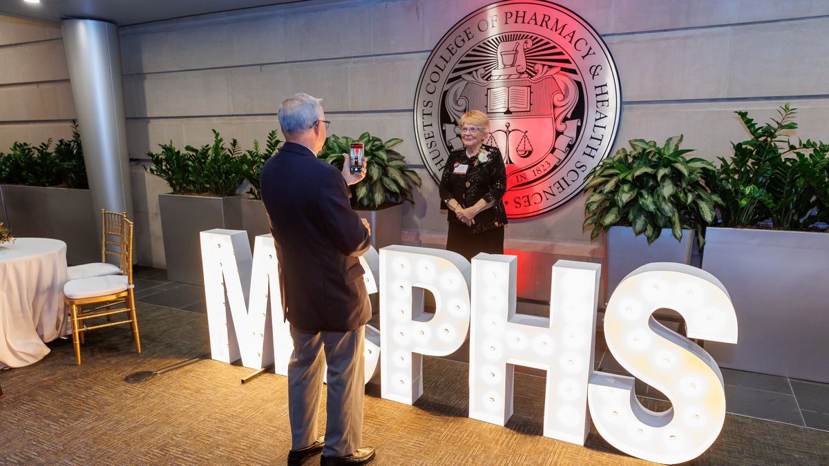 Ellen (Wheeler) Sylvia stands in front of the MCPHS seal.