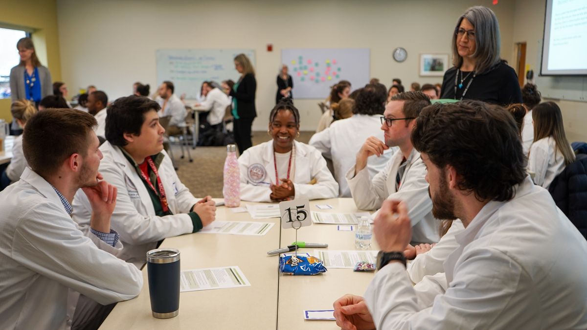MCPHS Students wearing lab coats sitting at a table.