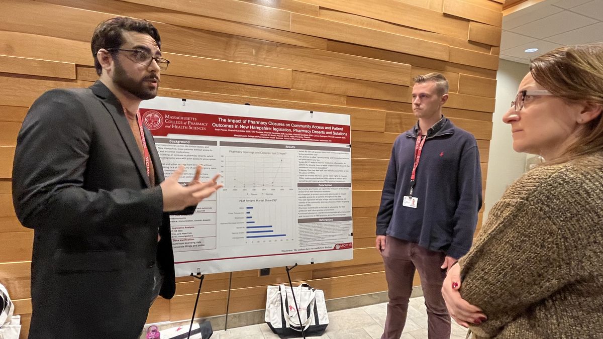 Two men and a woman stand in front of a poster and discuss.