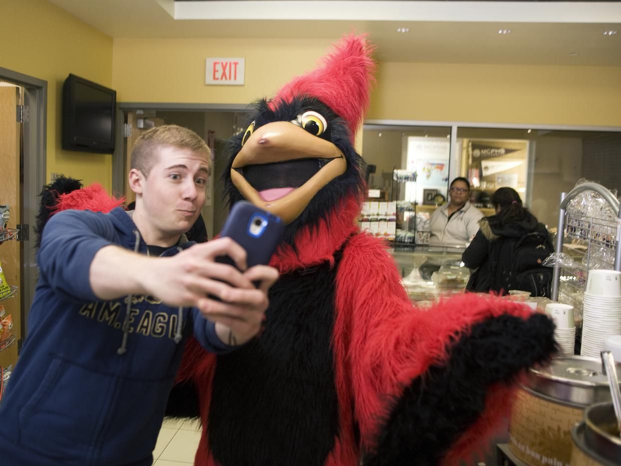 Student taking a selfie with Red the Cardinal.
