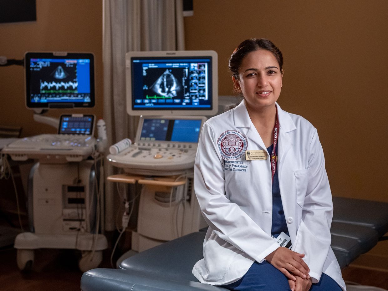 Female medical imaging student in white coat, sitting in front of MRI screen. 