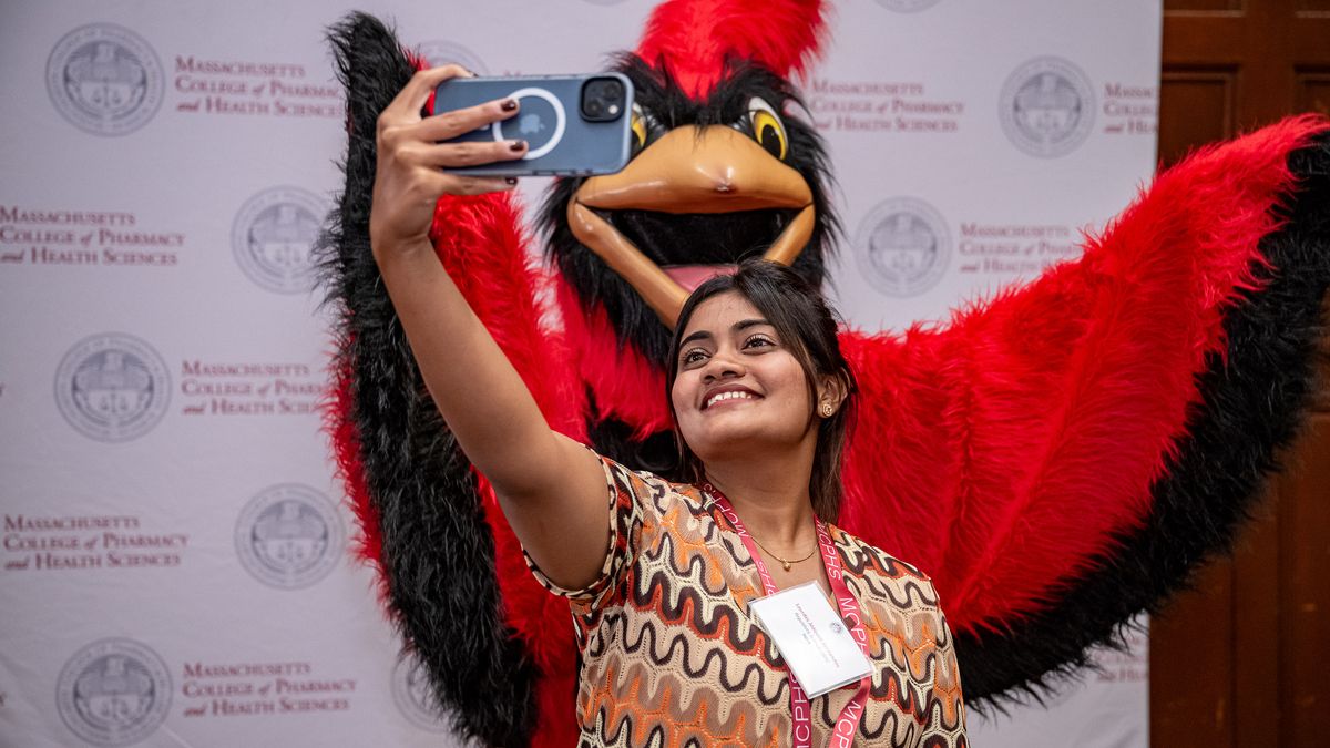 Woman takes a selfie with Red, the MCPHS mascot.