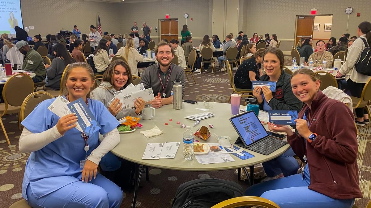 Five MCPHS students hold Be The Match registration kits, smiling for the camera