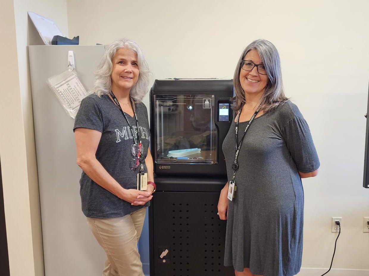 Dr. Michelle Dowling and Dr. Danielle Amero stand in front of a 3D printer.