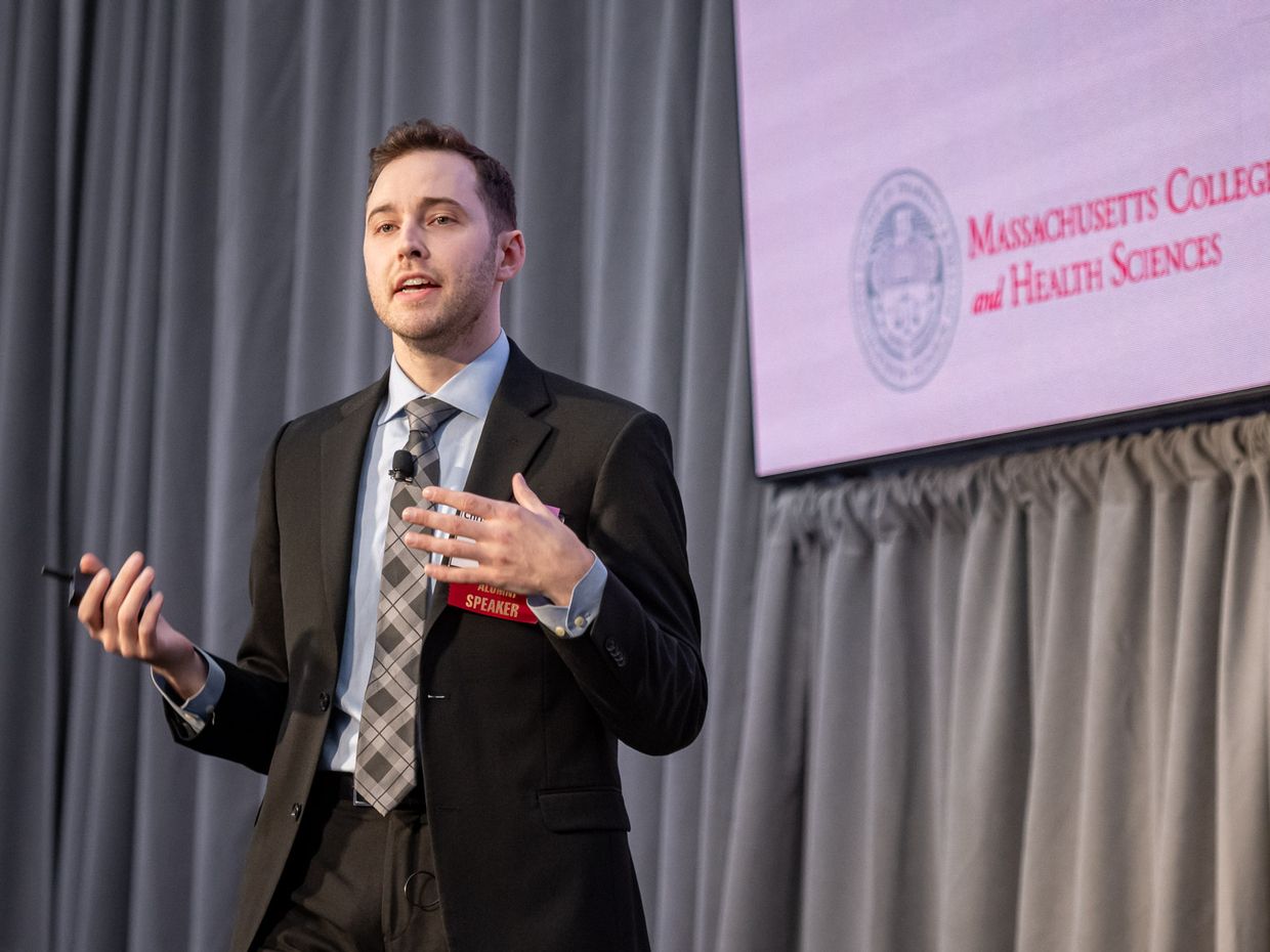 Male in business attire, speaking on a conference podium. 