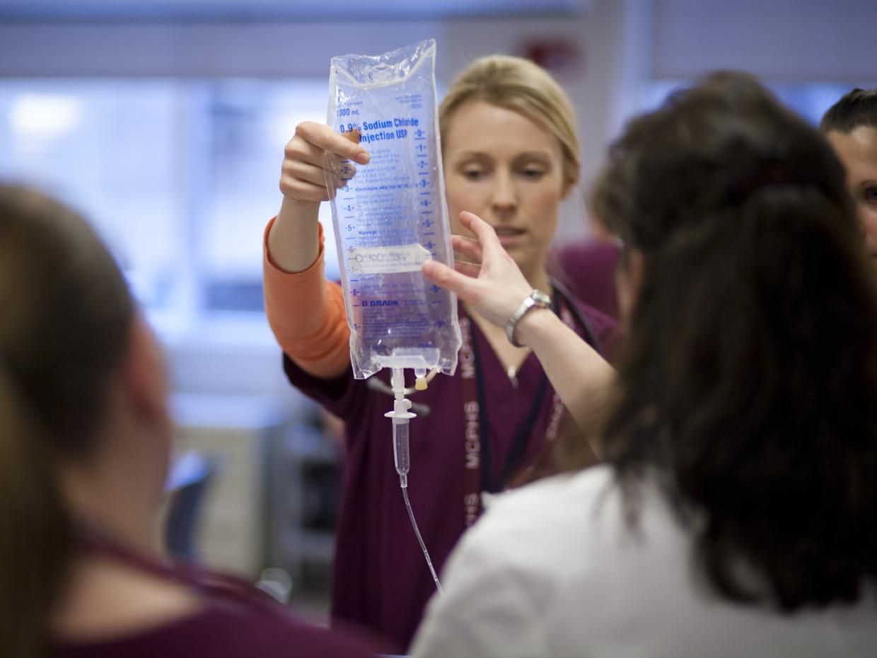 Female in scrubs holding an IV bag. 