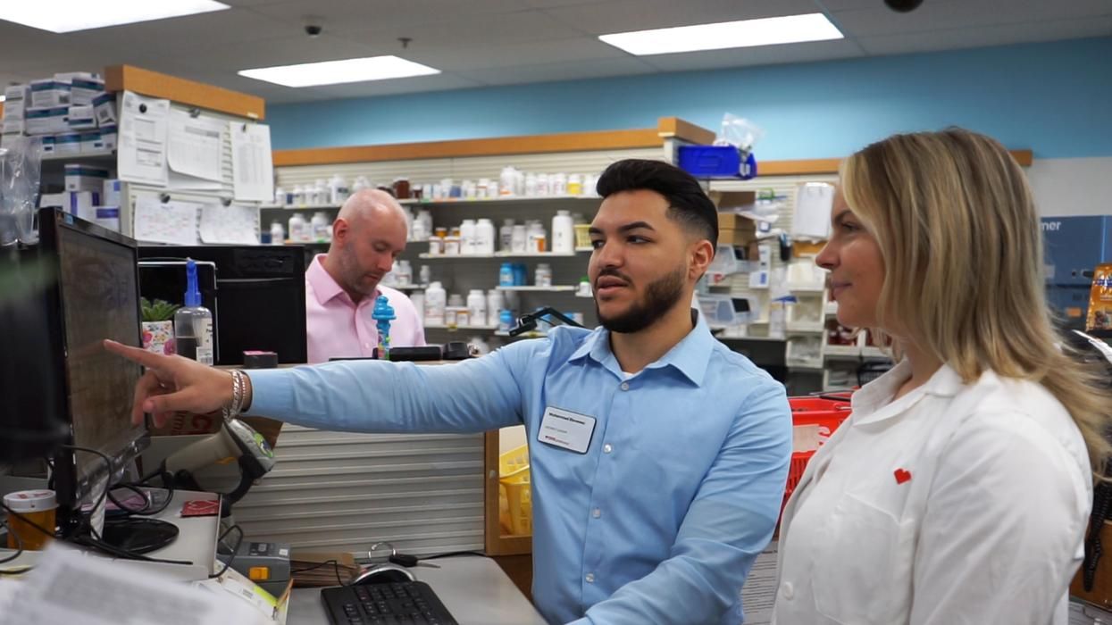 Muhammad Elsweesy looking at a computer in a pharmacy with a woman.