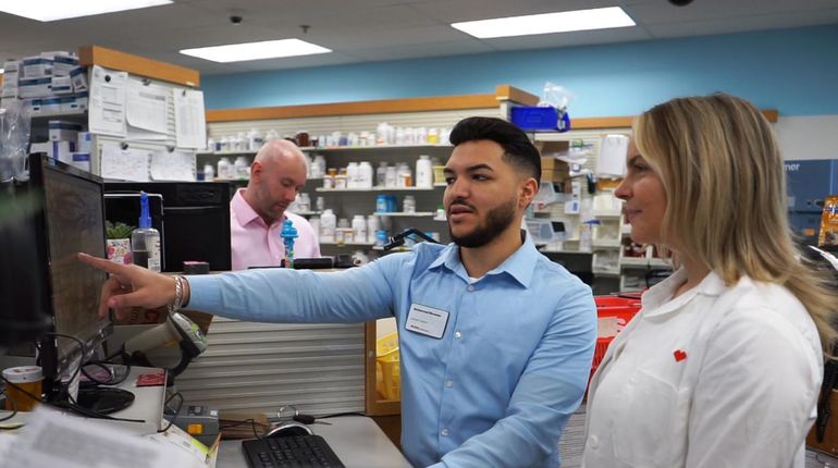 Muhammad Elsweesy looking at a computer in a pharmacy with a woman.