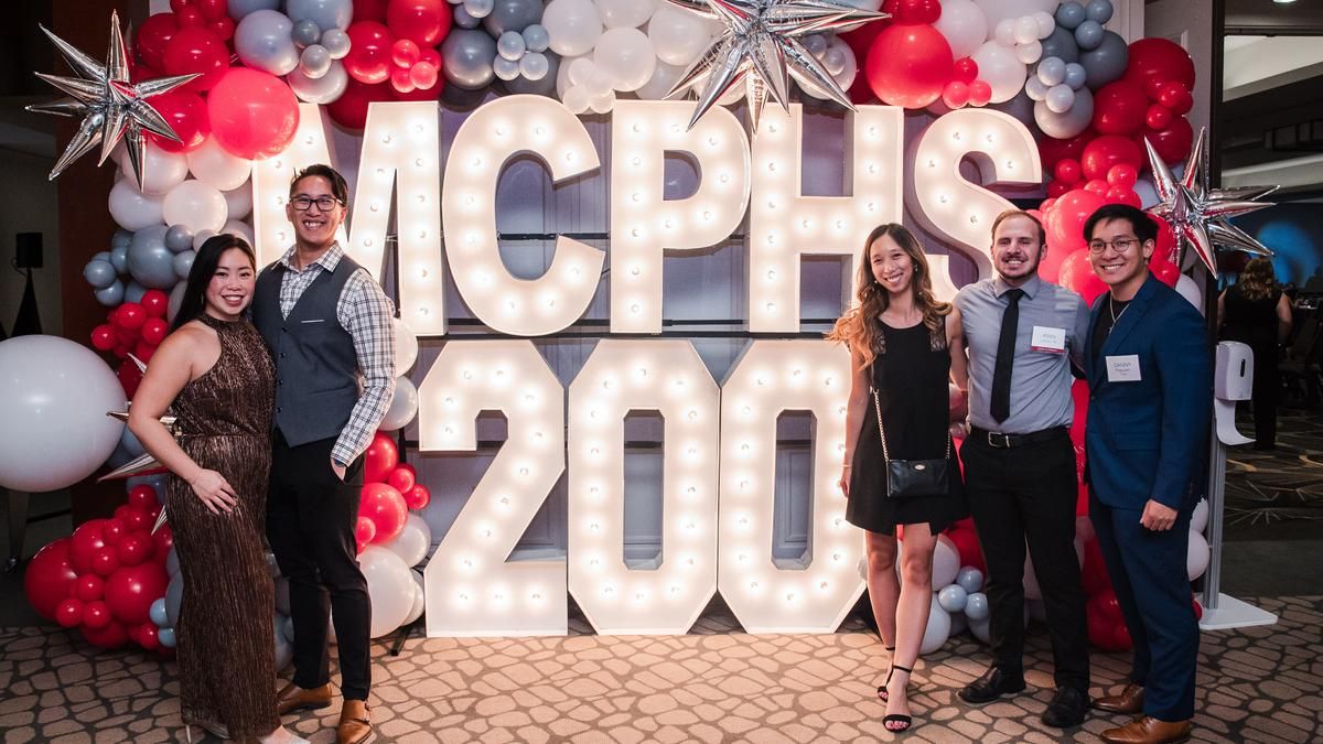 Alumni stand in front of the MCPHS 200 lights.