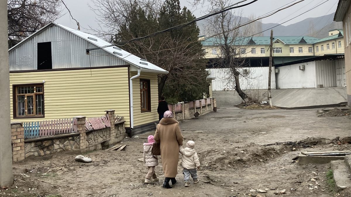 A woman and two children walk by a yellow building.