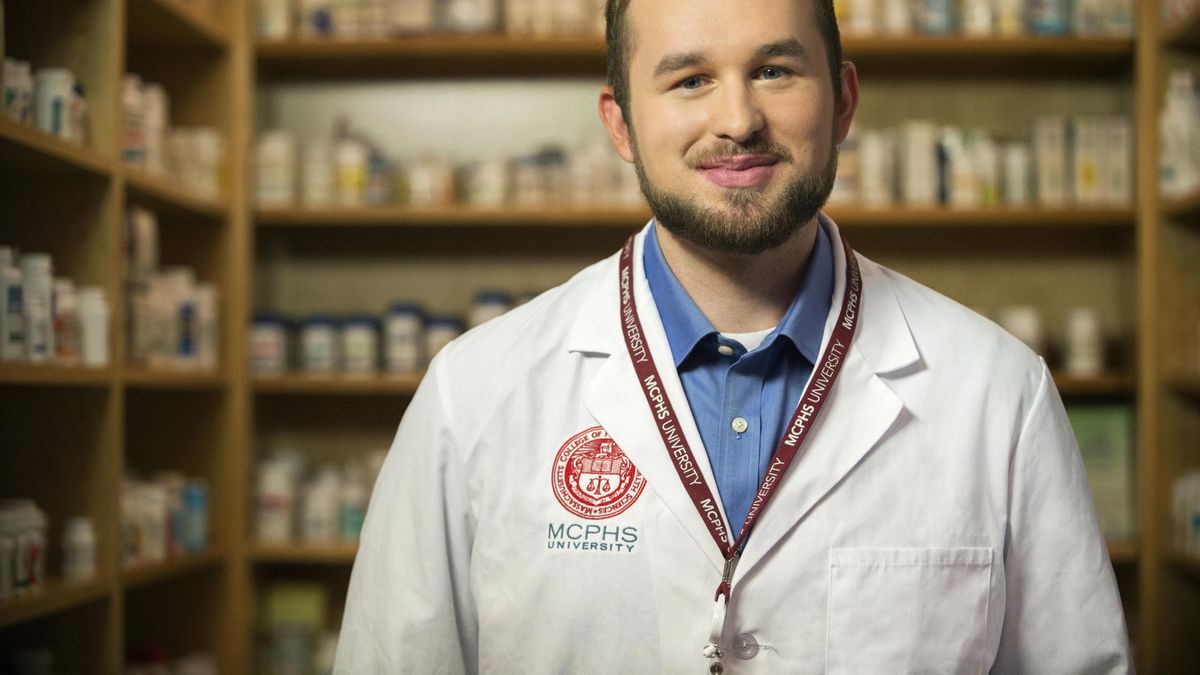 Smiling male student wearing a white lab coat in the pharmacy lab. 