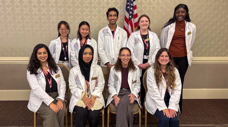 Nine students from Massachusetts College of Pharmacy and Health Sciences (MCPHS) smiling before a presentation on falls awareness.