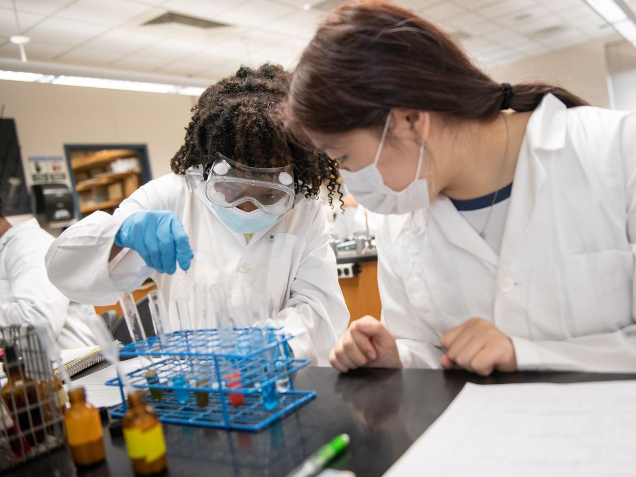 two students in lab coats working in a lab.	