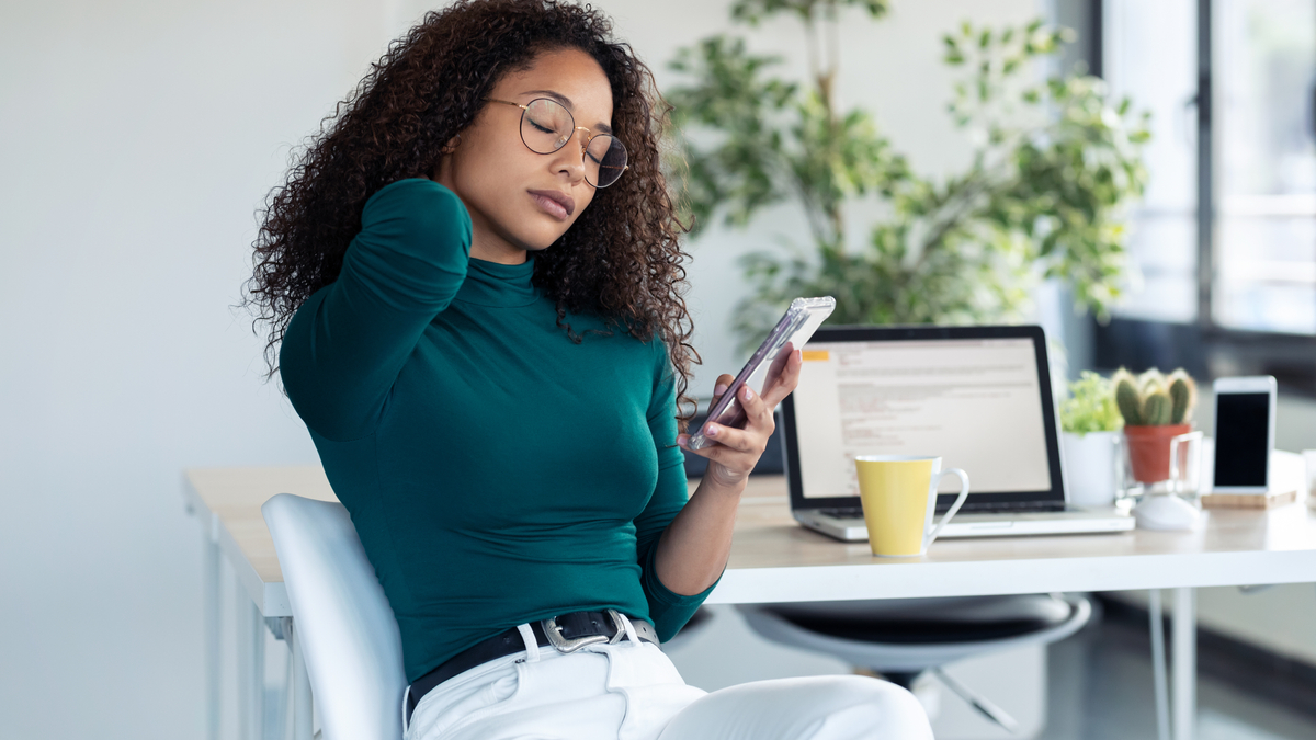 Woman holds neck while looking at phone.
