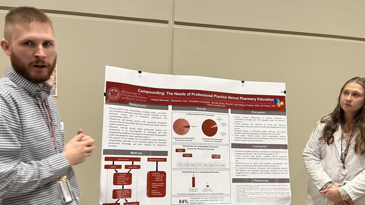 A woman and a man stand in front of a poster.