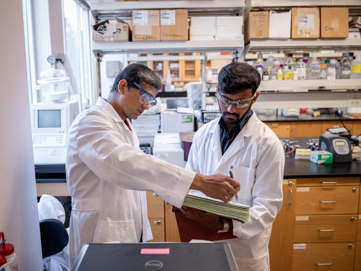 Faculty and student in white coats in lab talking. 