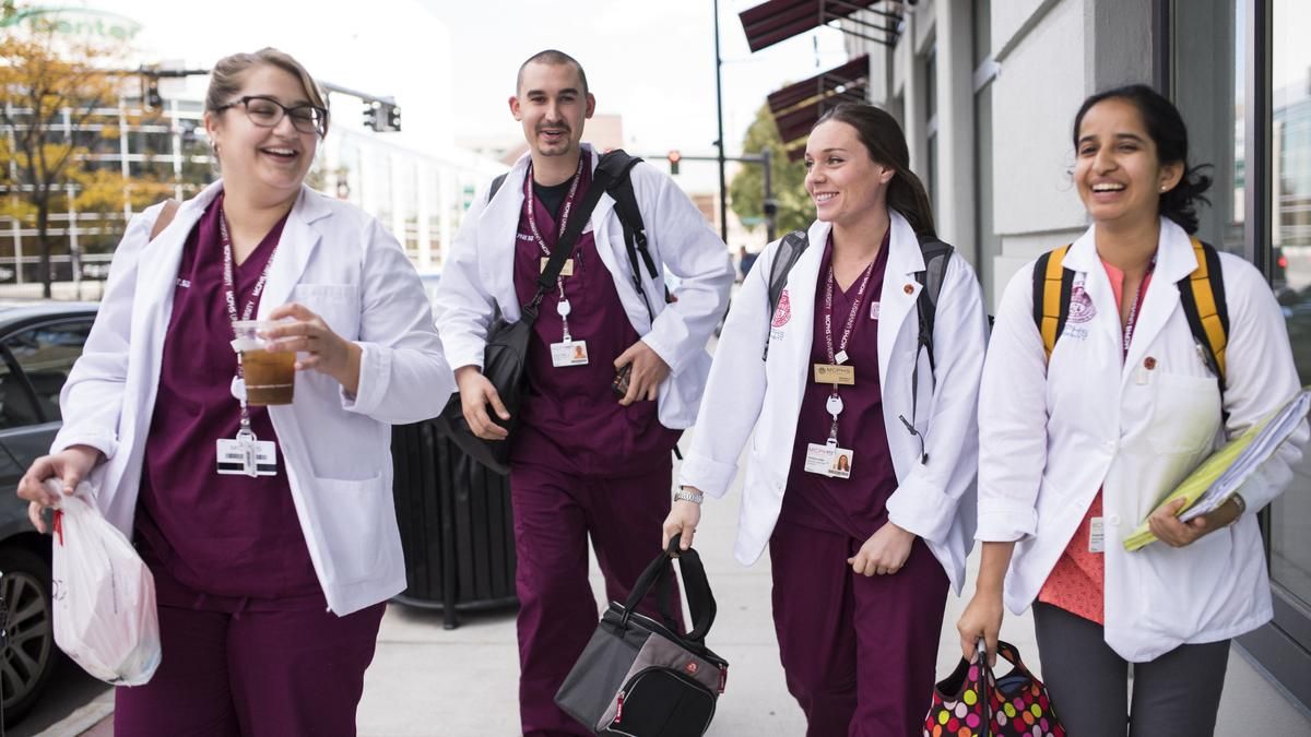 Four students in scrubs walking down the street and laughing. 