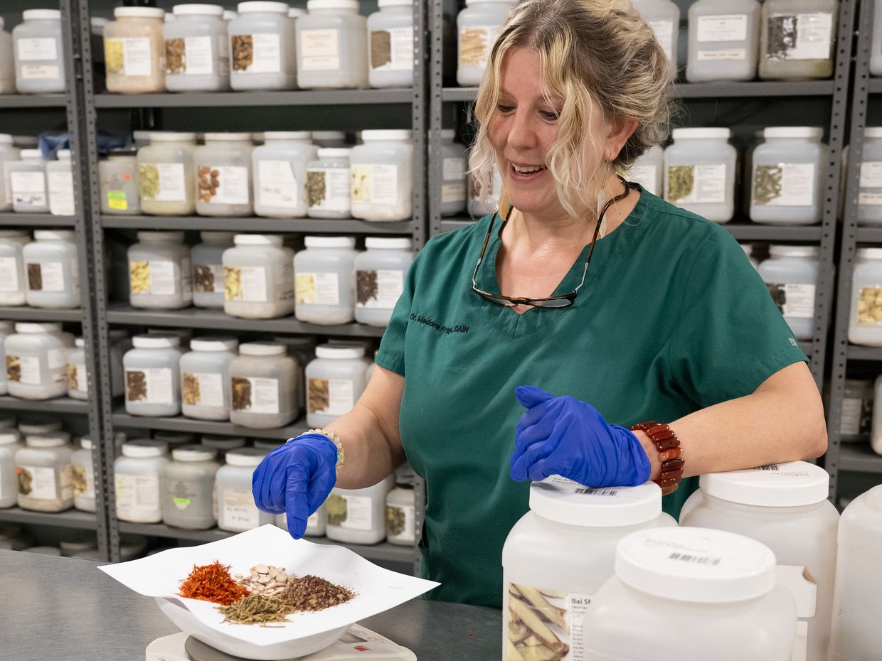 Acupuncture student in green scrubs measuring Chinese herbs. 