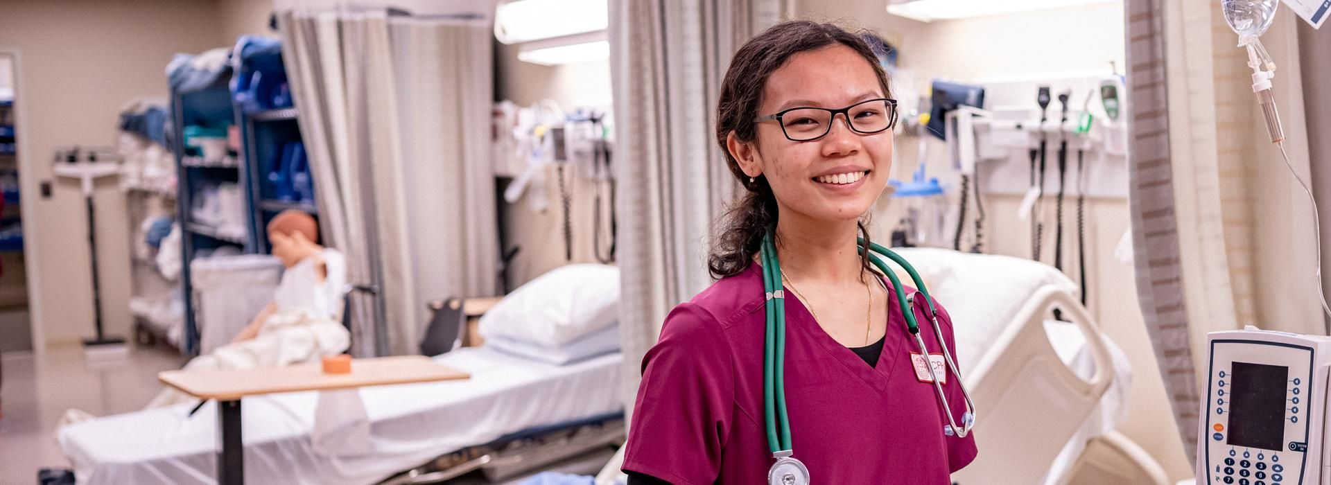 Female nursing student in scrubs, smiling. 