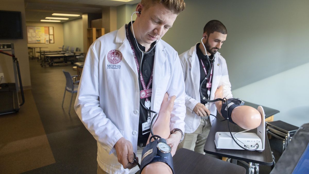 Two male students in white coats working on mannequin arms..jpg