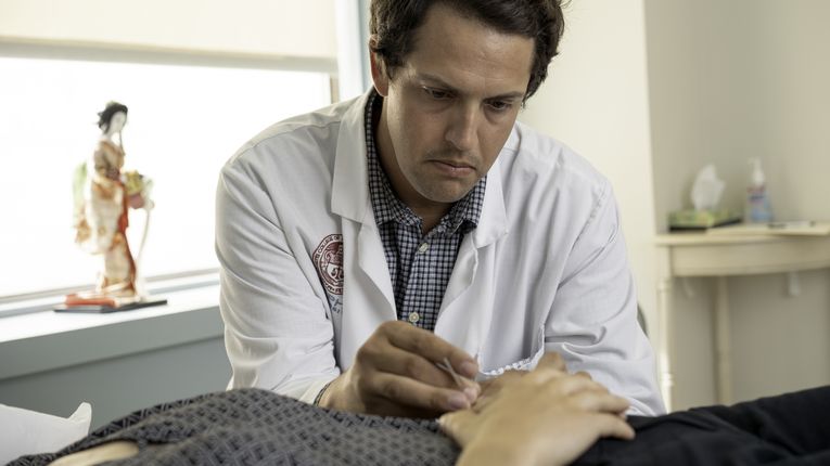 Acupuncture student inserting a needle into a patients hand. 