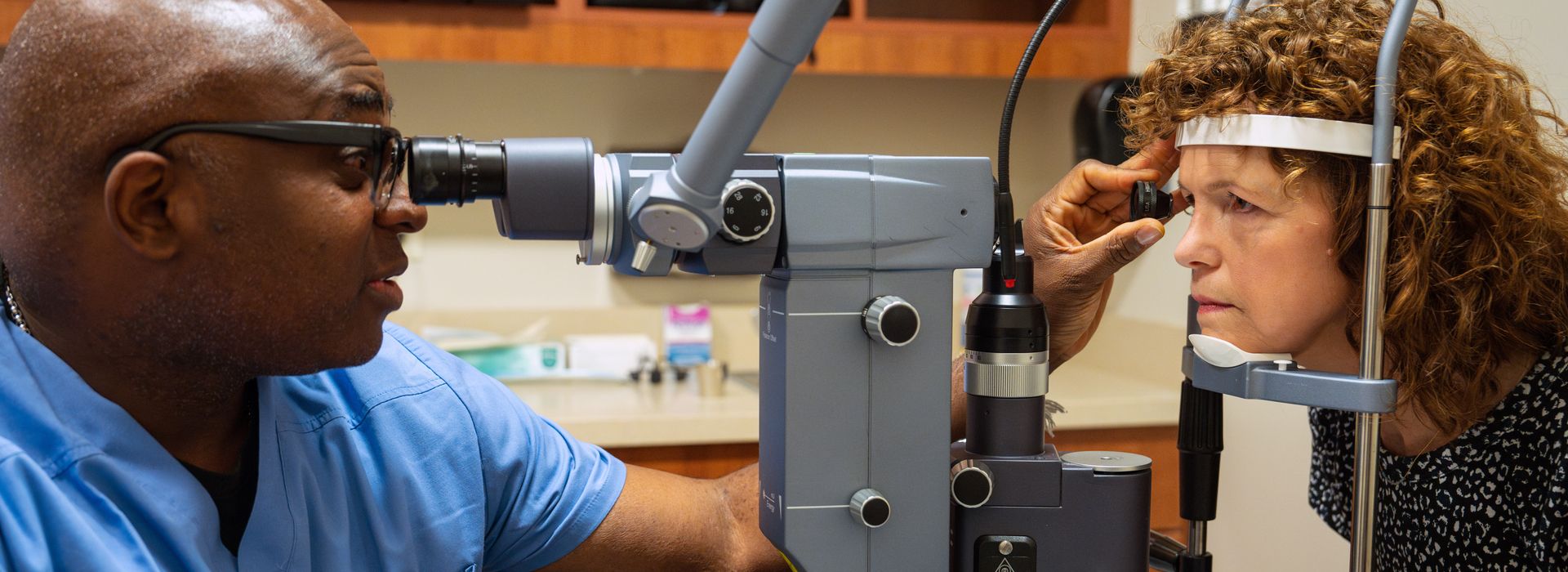 Close-up of an optometry student performing an eye exam on a patient using specialized diagnostic equipment in a clinical setting.