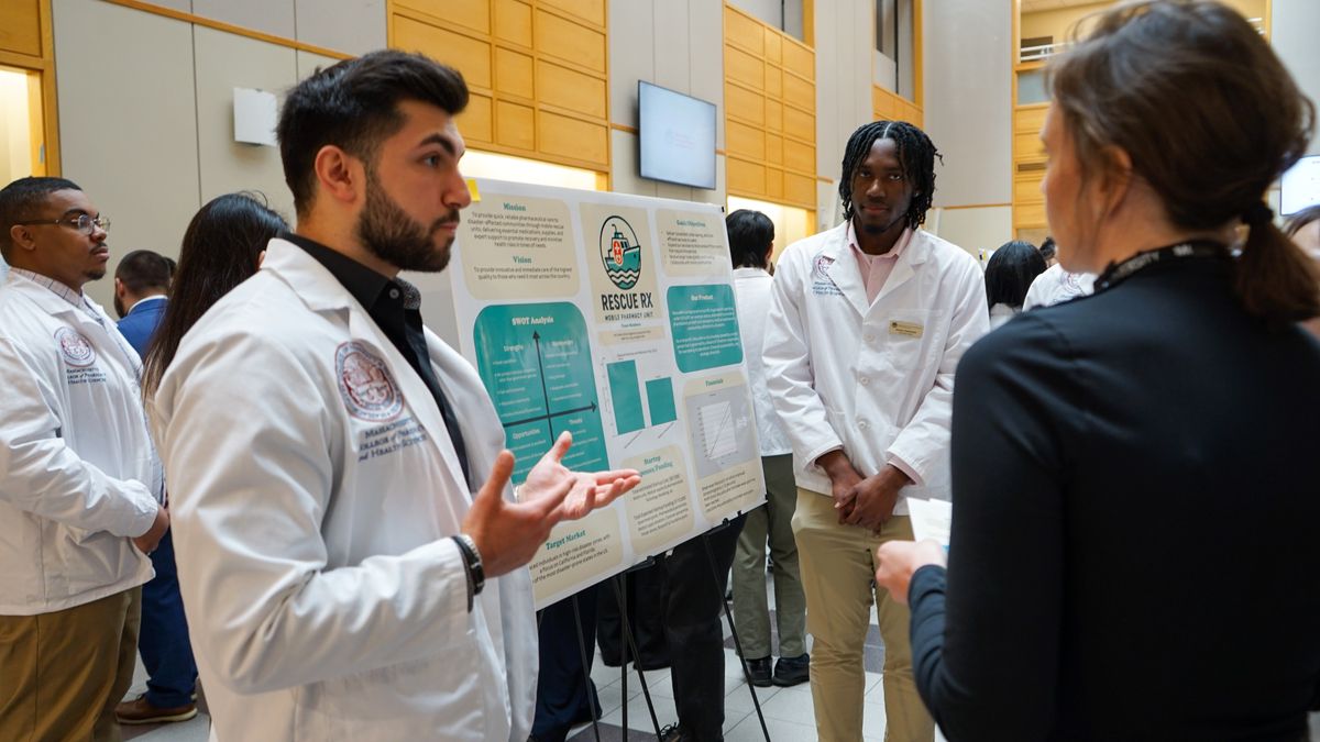 People standing in front of a poster at the MCPHS Boston Capstone Business Plan Competition.