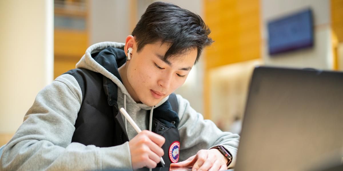 Male student sitting in front. of a laptop writing. 