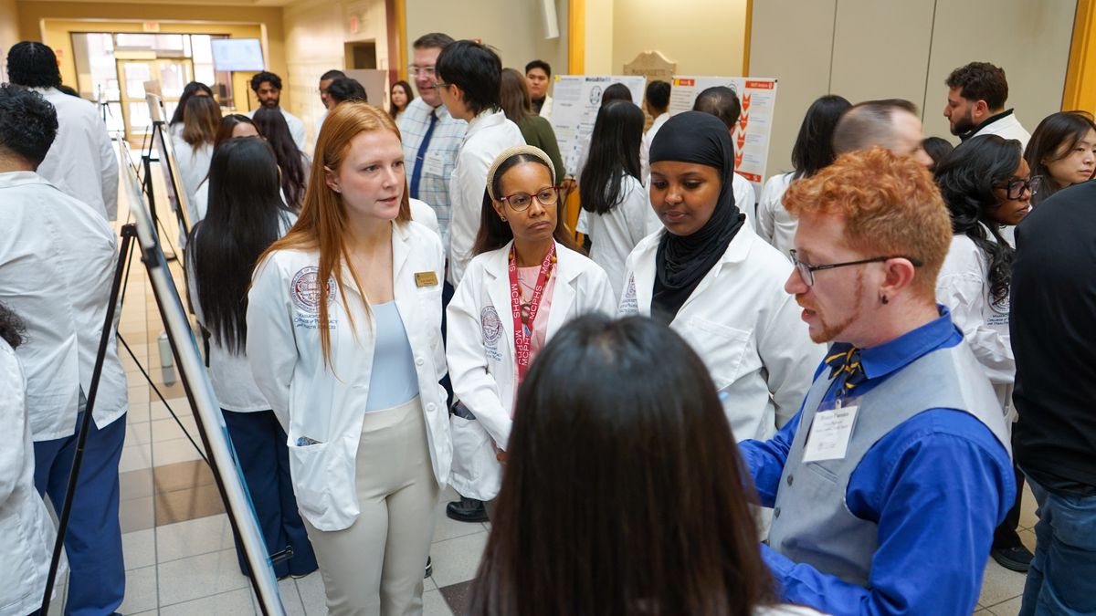 People standing in front of a poster at the MCPHS Boston Capstone Business Plan Competition.