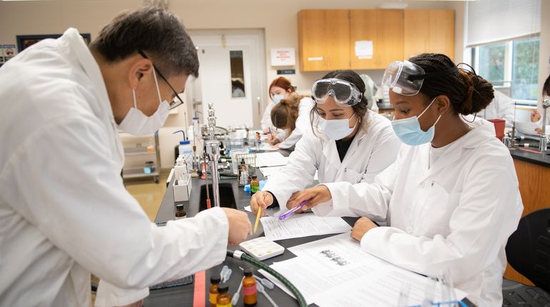 Students in white coats in the chemistry lab. 