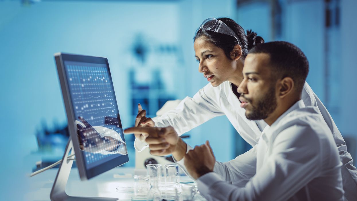 Man and woman in white coats pointing at a computer screen. 