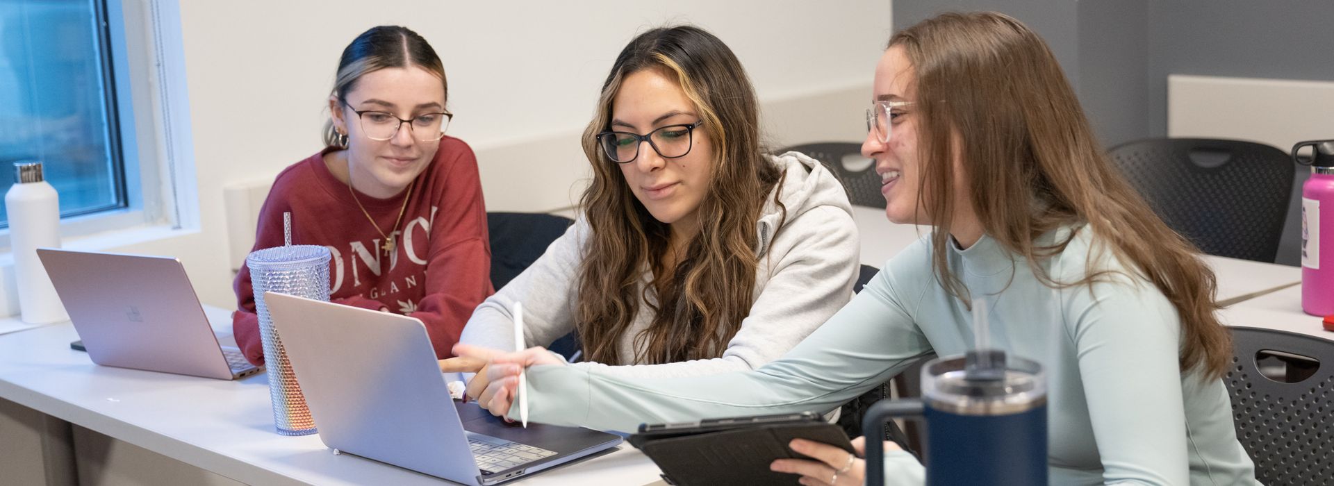 Three MCPHS students in a classroom looking at a laptop. 