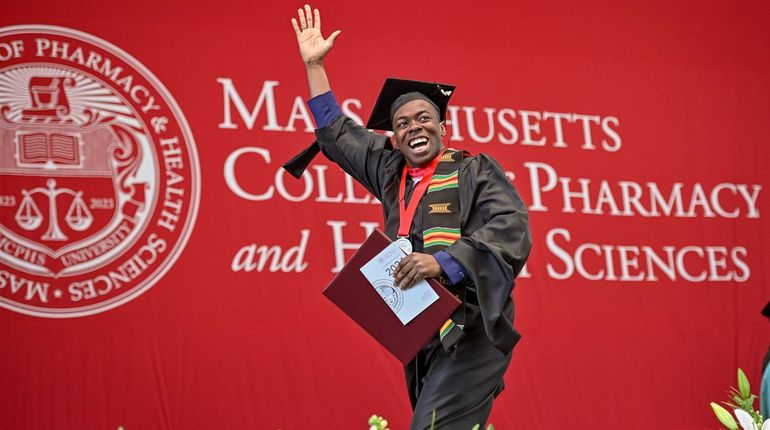 A male student walks across the stage at MCPHS commencement.