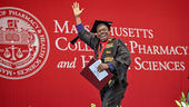 A male student walks across the stage at MCPHS commencement.