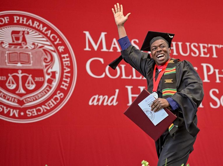 A male student walks across the stage at MCPHS commencement.