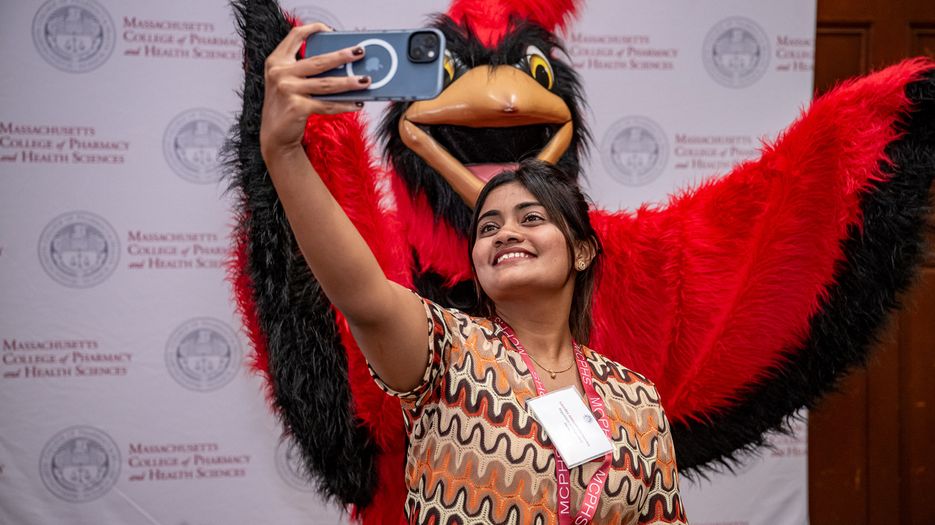 Woman takes a selfie with Red, the MCPHS mascot.