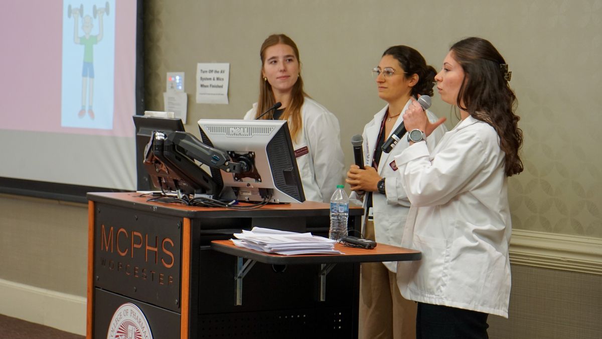 Three MCPHS students stand at the podium at the IPE Fall Awareness event.