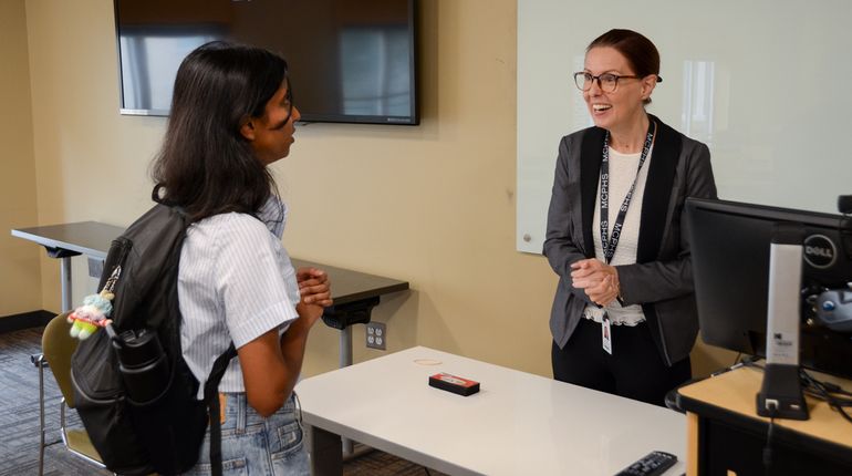 Professor speaks to student in classroom.