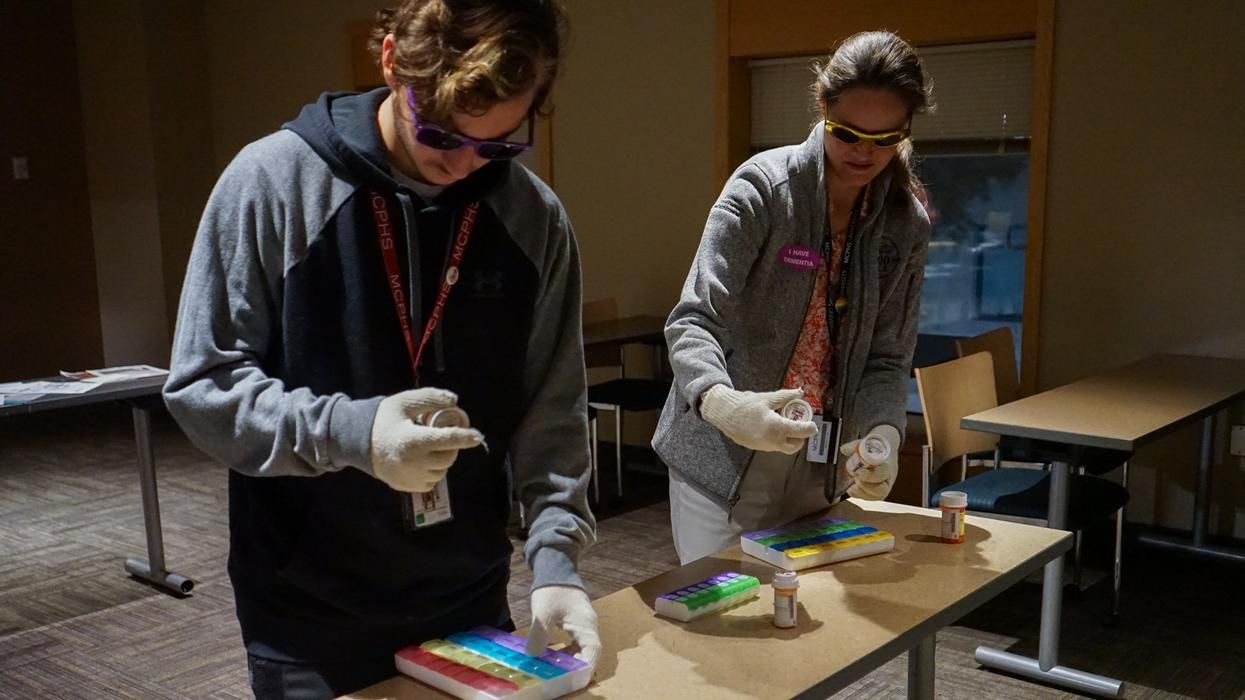 Two people in a lab wearing glasses looking at medicine.