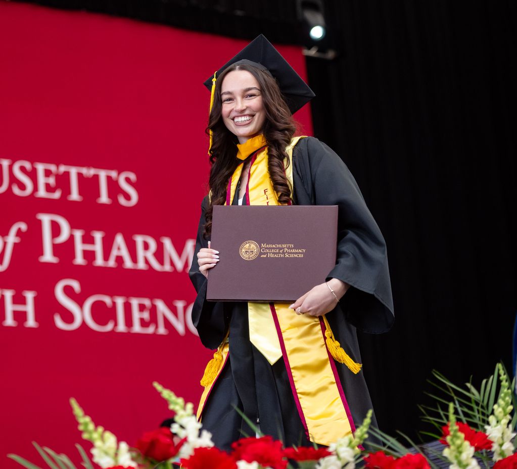 MCPHS student holding diploma at May 2026 graduation. 