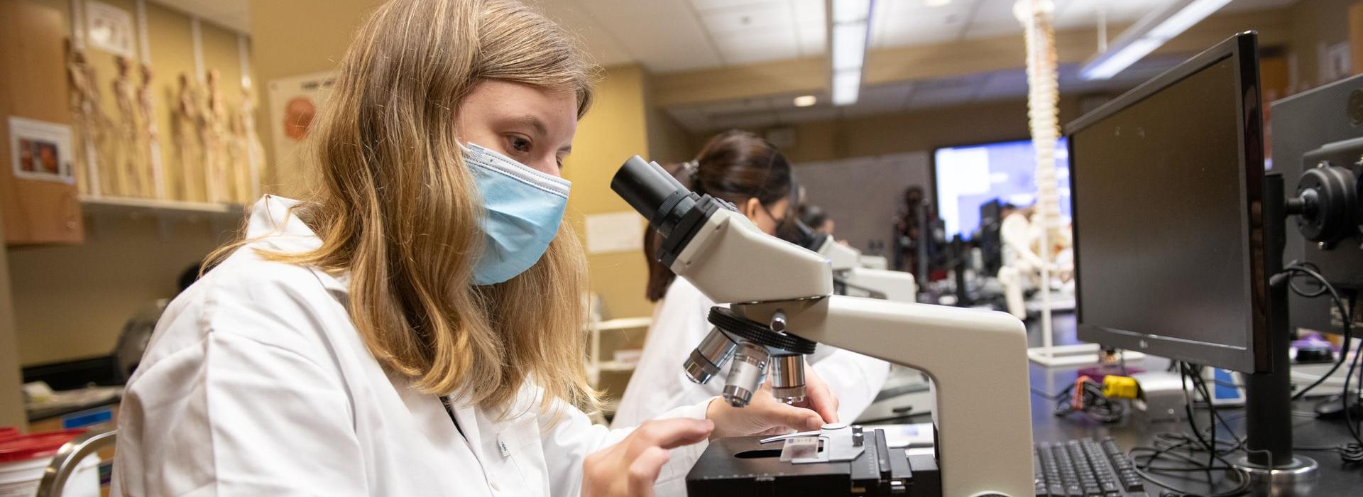 Female student looking through microscope in a lab. 
