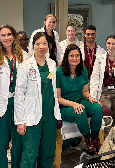 A group of students from MCPHS, most wearing white coats, stand next to each other and smile for a photo.