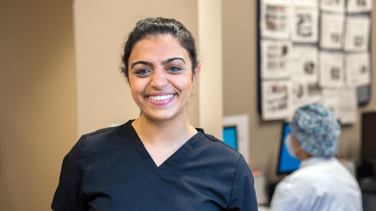 Smiling female dental hygiene student in blue scrubs.