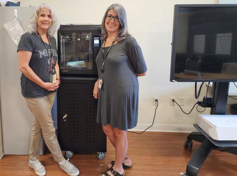 Dr. Michelle Dowling and Dr. Danielle Amero stand in front of a 3D printer.