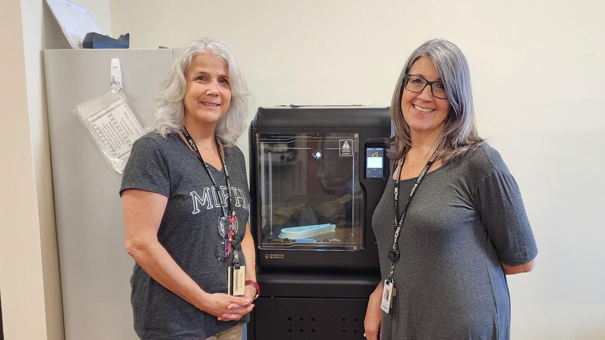 Dr. Michelle Dowling and Dr. Danielle Amero stand in front of a 3D printer.