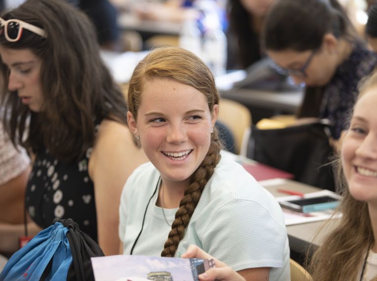 Smiling girl sitting in classroom with other students.