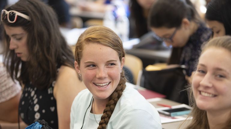 Smiling girl sitting in classroom with other students.