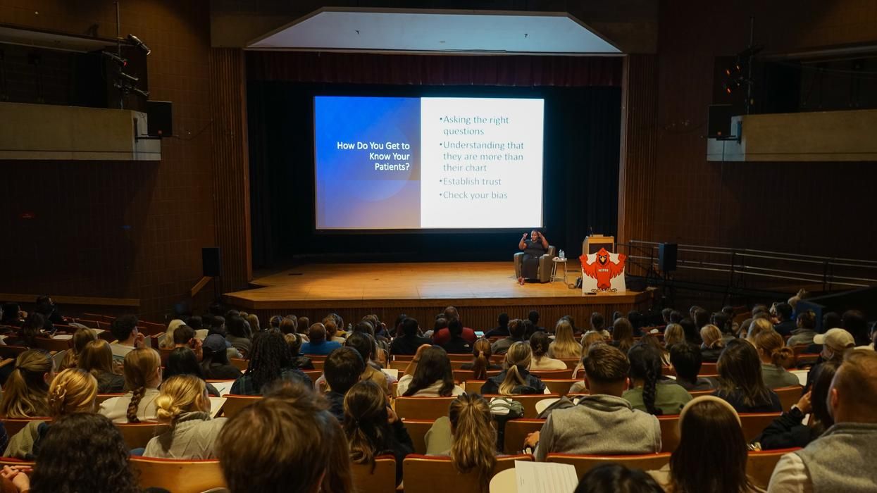 Emma Sellers, MS, sits on stage while presenting to an audience of PA students from MCPHS