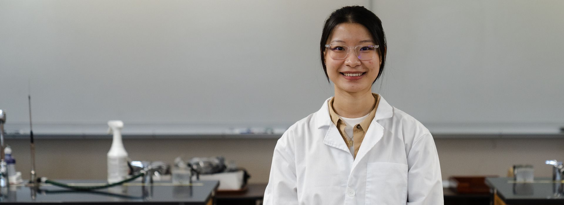 Smiling female student in a white lab coat. 